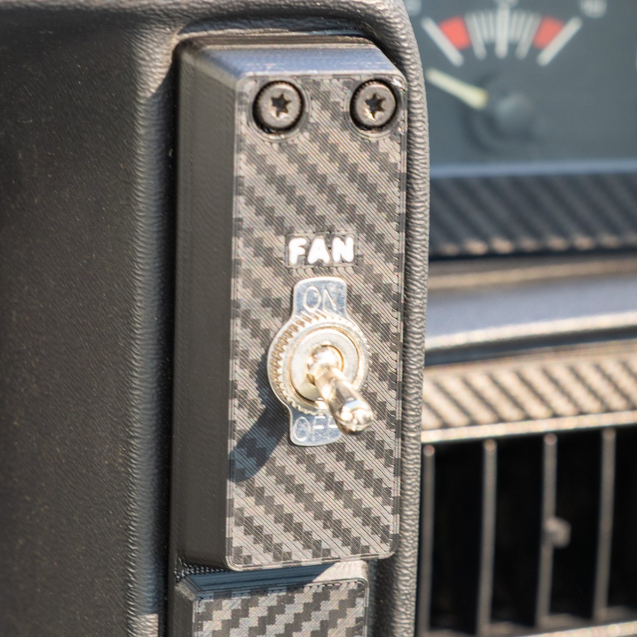 Reproduction Fiero passenger-side cluster panel installed, with an engine fan toggle switch and FAN inlaid in white above it