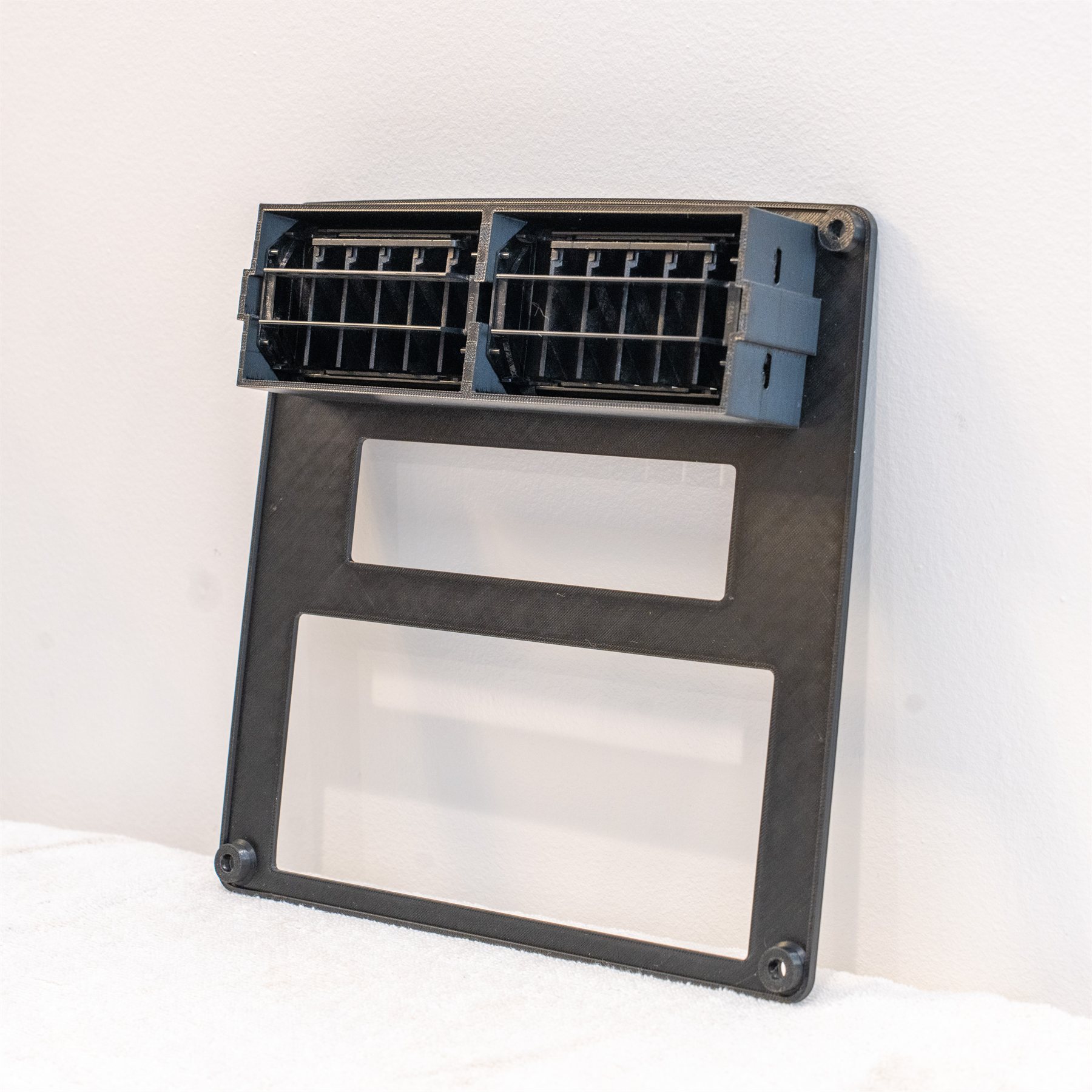 Rear view of a reproduction Fiero stereo bezel with the factory air vents snapped in